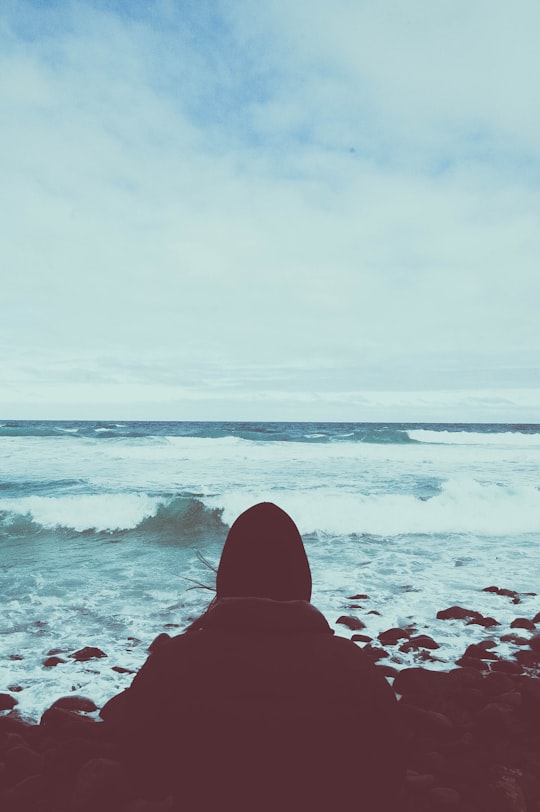 person sitting on rocking shore under cloudy sky in Boulder Beach New Zealand