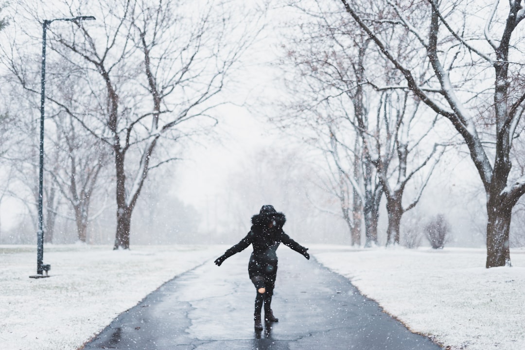 woman wearing black parka jacket standing on road near tall trees and light post during daytime