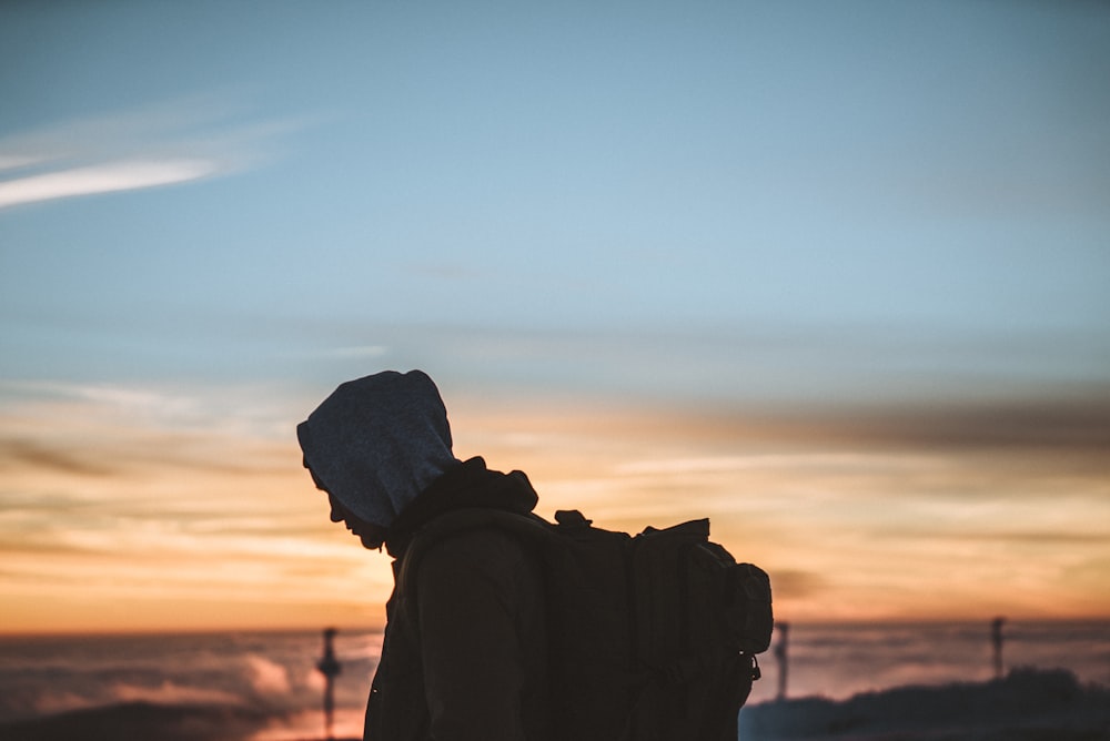 silhouette of person carrying backpack during orange sunset