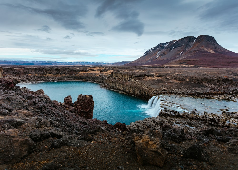 body of water near mountain under white clouds at daytime