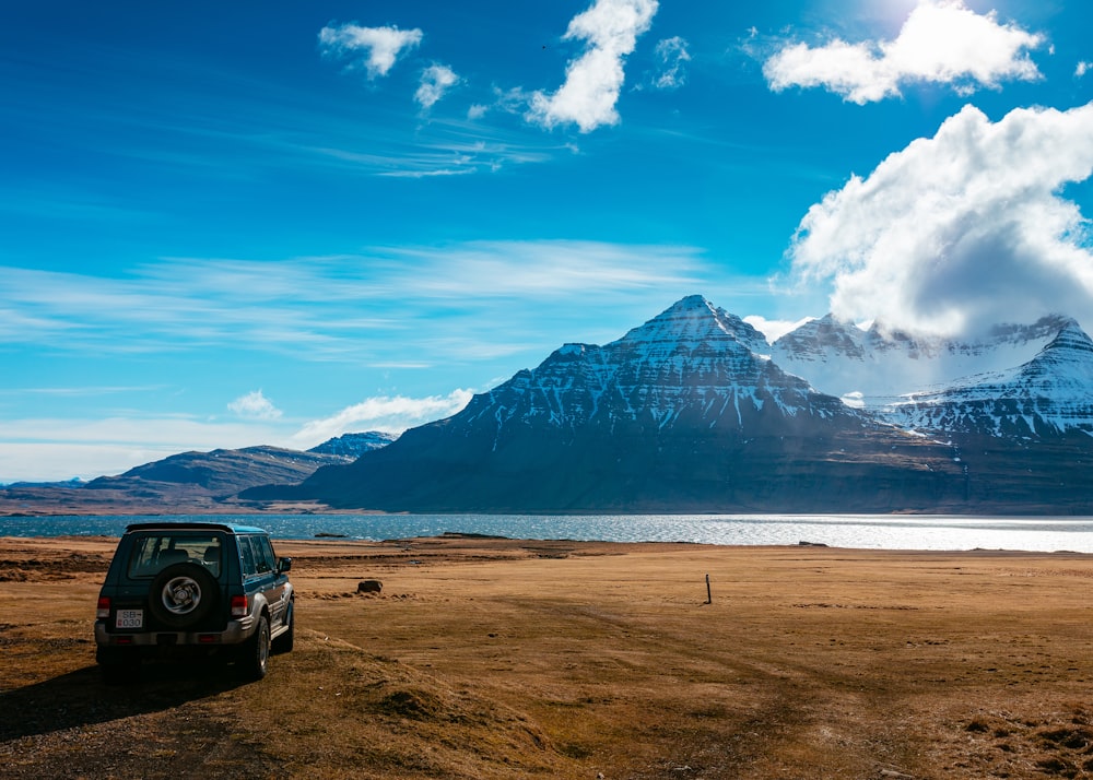 Estacionamento de SUV em campo marrom de frente para o lago em toda a montanha preta coberta de neve durante o dia