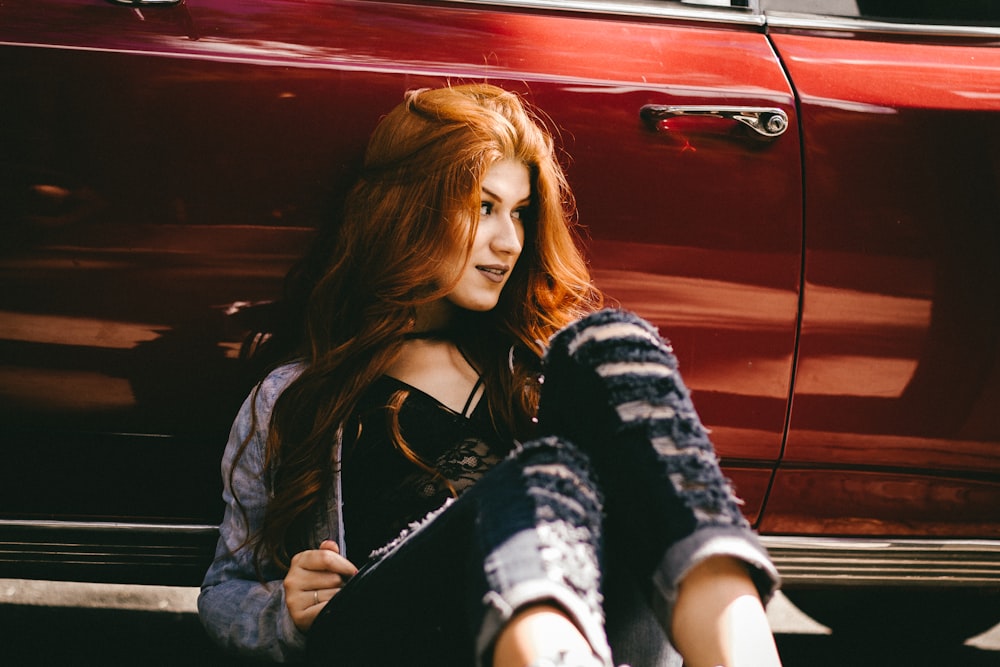 femme souriante assise à côté d’une voiture rouge