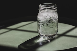 A clear water container filled with fresh water, placed on a wooden table under natural sunlight.