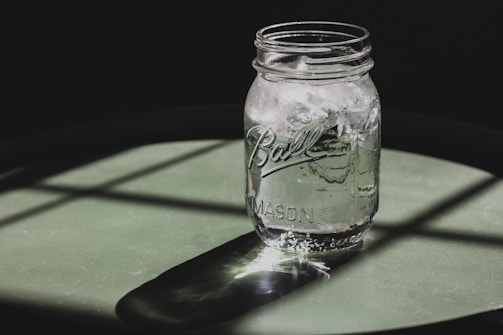 A clear water container filled with fresh water, placed on a wooden table under natural sunlight.