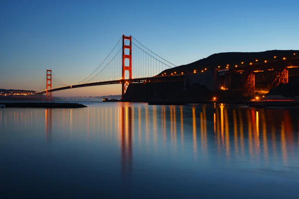 The Golden Gate Bridge at dusk with lights reflected in the bay