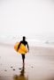 man holding yellow surfboard while walking on seashore during daytime