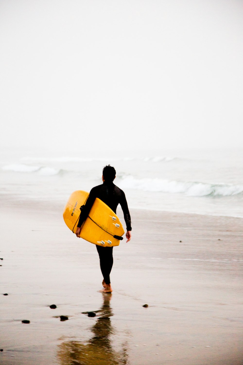 uomo che tiene la tavola da surf gialla mentre cammina in riva al mare durante il giorno
