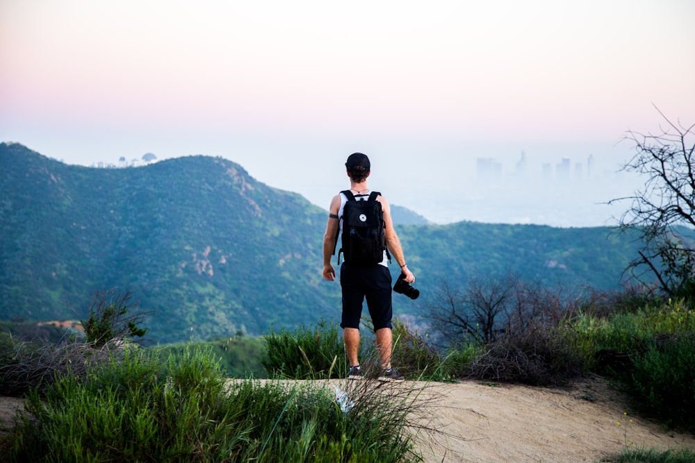 man wearing black backpack standing near mountain at daytime