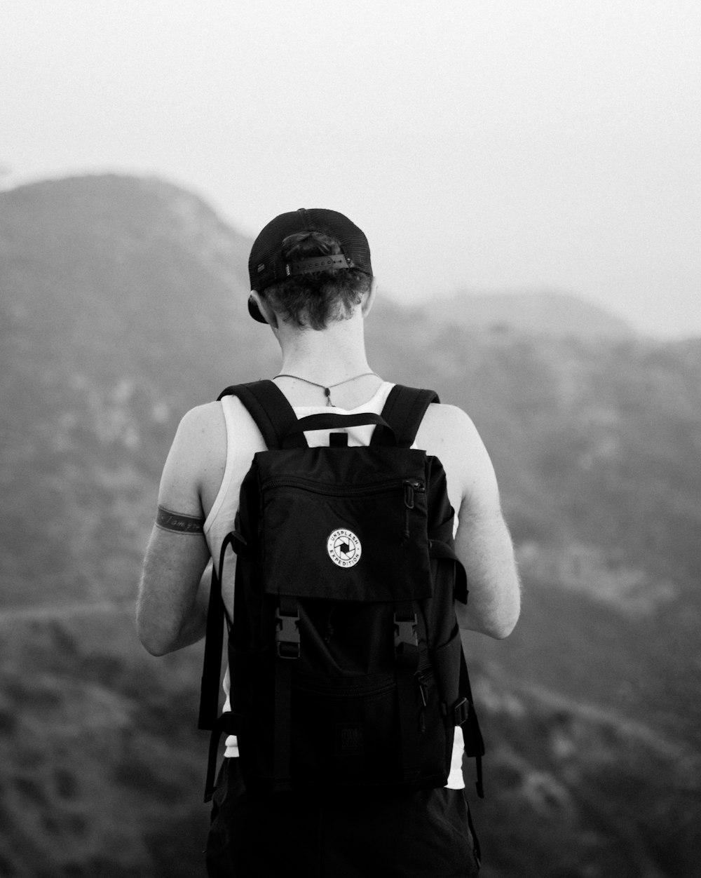 man standing facing mountains wearing backpack
