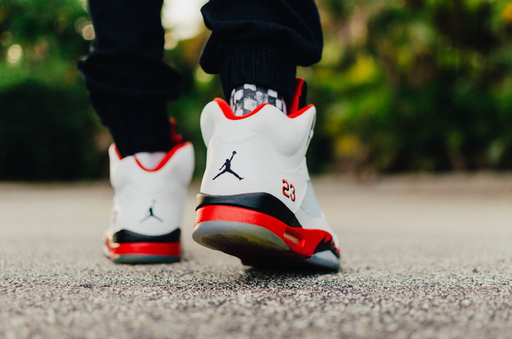 personne portant des chaussures Air Jordan 5 blanches, noires et rouges