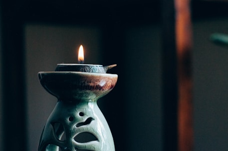Close-up of a beautifully crafted decorative candle with soft glowing flame on a rustic wooden table.