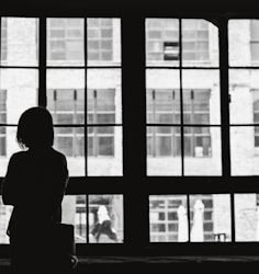 grayscale photography of woman facing window