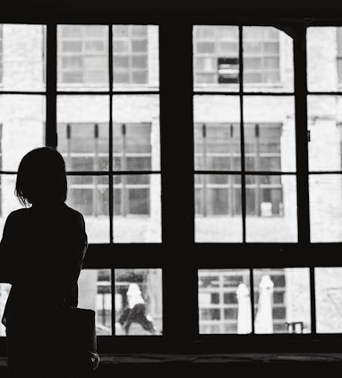 grayscale photography of woman facing window