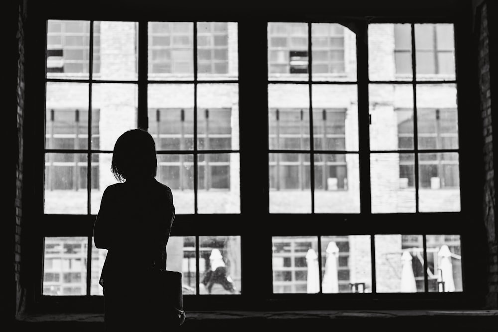 Fotografía en escala de grises de mujer frente a la ventana