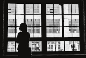 Uma mulher observando o ambiente externo através de uma janela com grades 