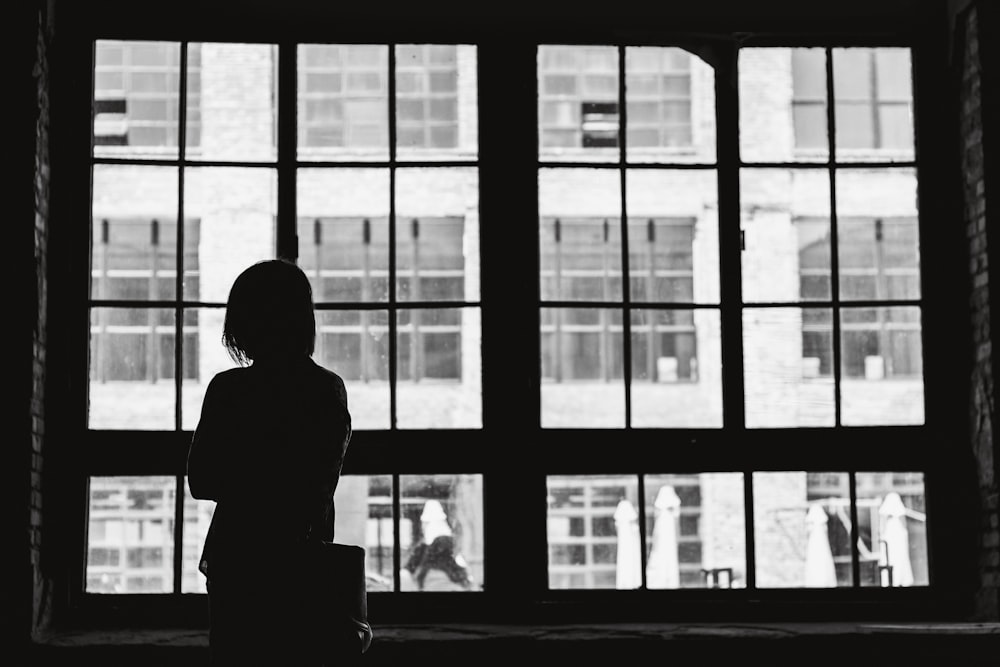 grayscale photography of woman facing window