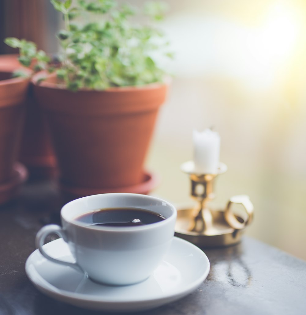 weiße Keramiktasse gefüllt mit schwarzer Flüssigkeit auf der Untertasse