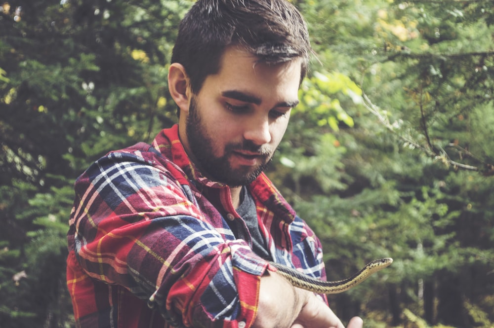 man holding black and white snake outdoor during daytime