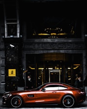 red coupe parked in front of black and gray building during daytime