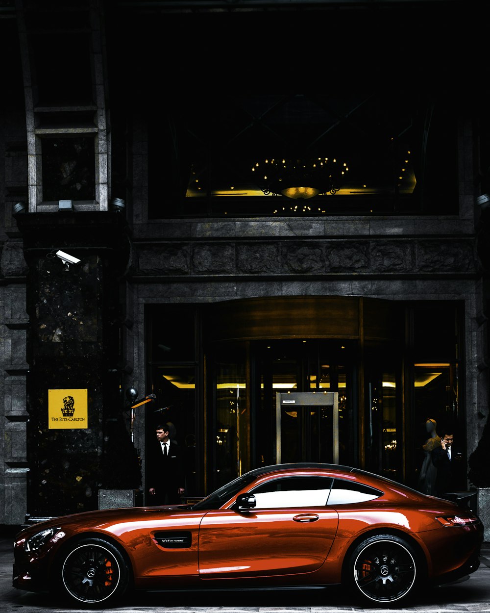coupé rossa parcheggiata di fronte all'edificio nero e grigio durante il giorno