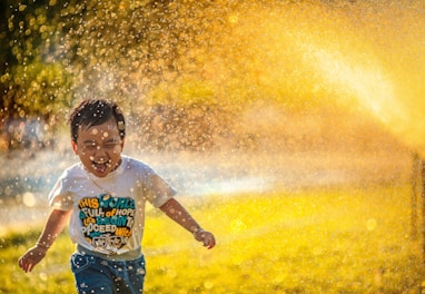 a young boy running through a sprinkle of water