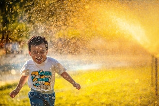 a young boy running through a sprinkle of water