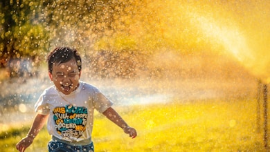 a young boy running through a sprinkle of water