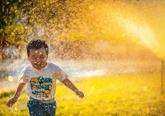 a young boy running through a sprinkle of water