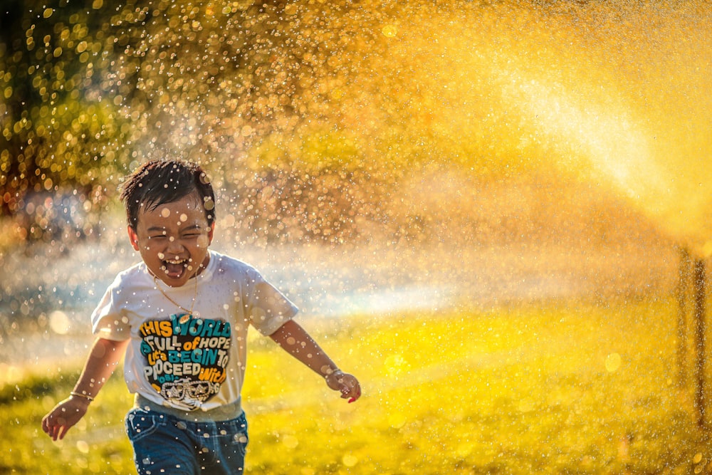 a young boy running through a sprinkle of water