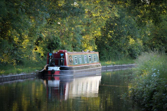 A sleek turquoise electric canal boat gliding smoothly along a peaceful historic canal under soft sunlight.