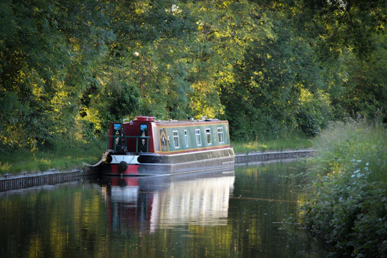 A sleek turquoise electric canal boat gliding smoothly along a peaceful historic canal under soft sunlight.
