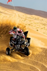 An ATV kicking up dust as it speeds across a rocky landscape.