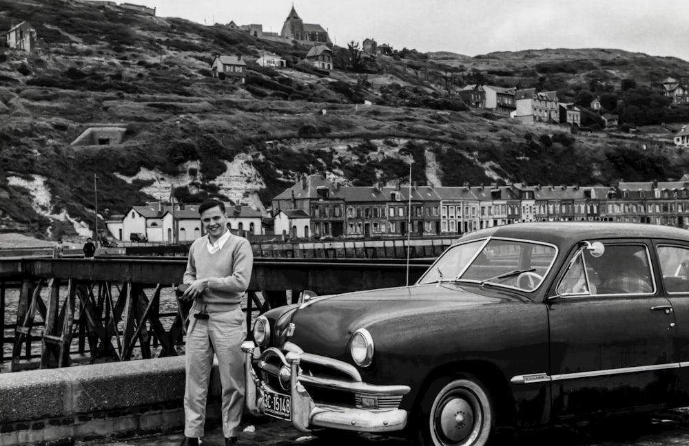 grayscale photography of man standing front of vehicle