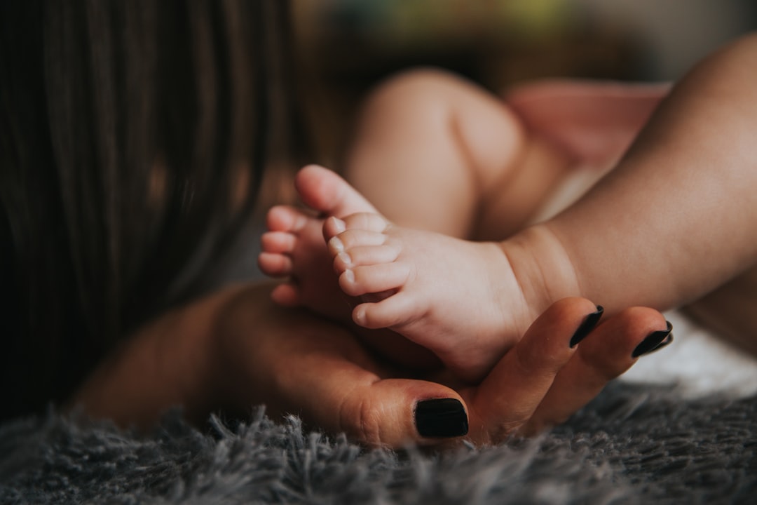 Infant's feet being held by a woman's hand with painted and manicured hands resting on a gray blanket