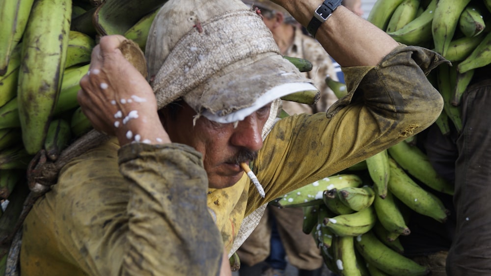 man with cigarette on mouth carrying bananas on his back