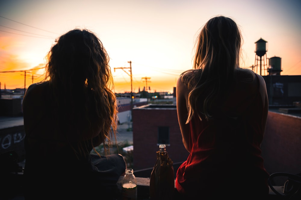 屋上に座り、夕日を眺める2人の女性