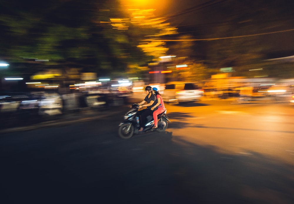 couple riding on black motor scooter during nighttime