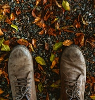 A pair of leather boots resting on a cobblestone path with autumn leaves.