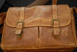 A close-up of a beautifully worn leather satchel with visible vintage stitching and patina.