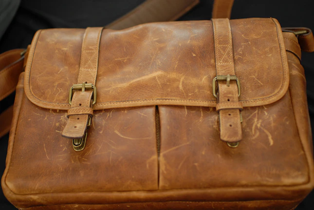 Close-up of a worn leather military satchel with brass buckles.