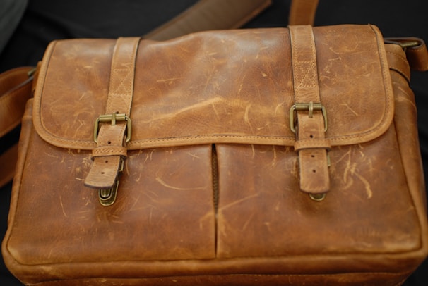 A vibrant leather messenger bag with brass buckles displayed on a rustic table.