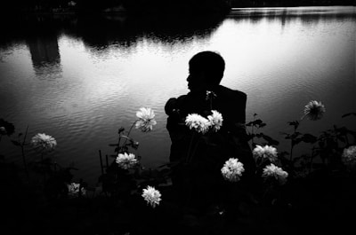 A solitary figure sitting by a calm lake at dusk, immersed in quiet reflection.