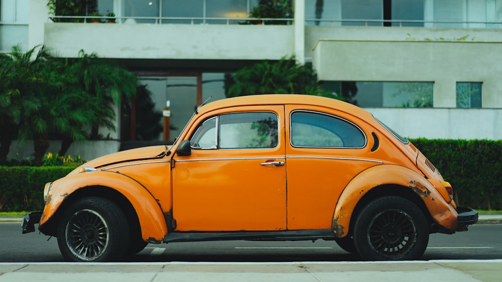 Rusted old vintage orange Volkswagen beetle parked in front of apartment complex