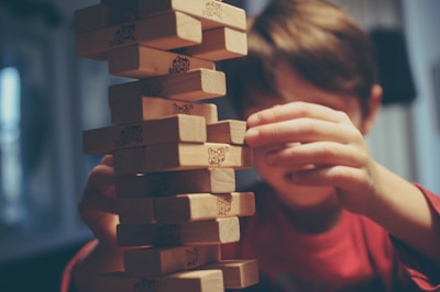 A close-up of small hands carefully placing a wooden block on a growing tower.