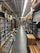 An aisle in a hardware store lined with shelves stocked with various products, including boxes, cans, and construction materials. The aisle is long and narrow, flanked by high shelves filled with merchandise. The ceiling features exposed utilities and fluorescent lighting.