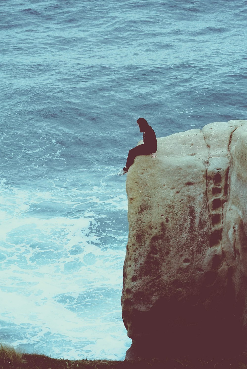 Persona che si siede sul bordo della roccia che guarda il mare