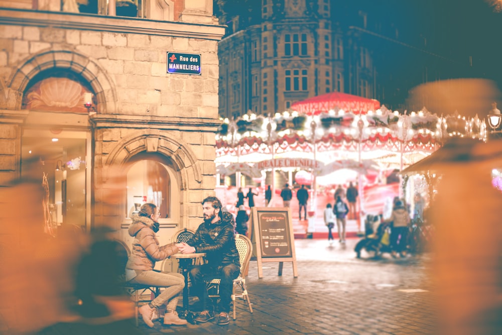 couple sitting beside building near carousel during night time