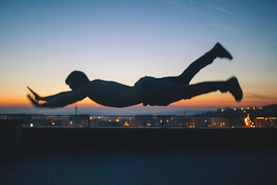 Keluang Man soaring over the Kuala Lumpur skyline at dusk, cape fluttering against the glowing city lights.