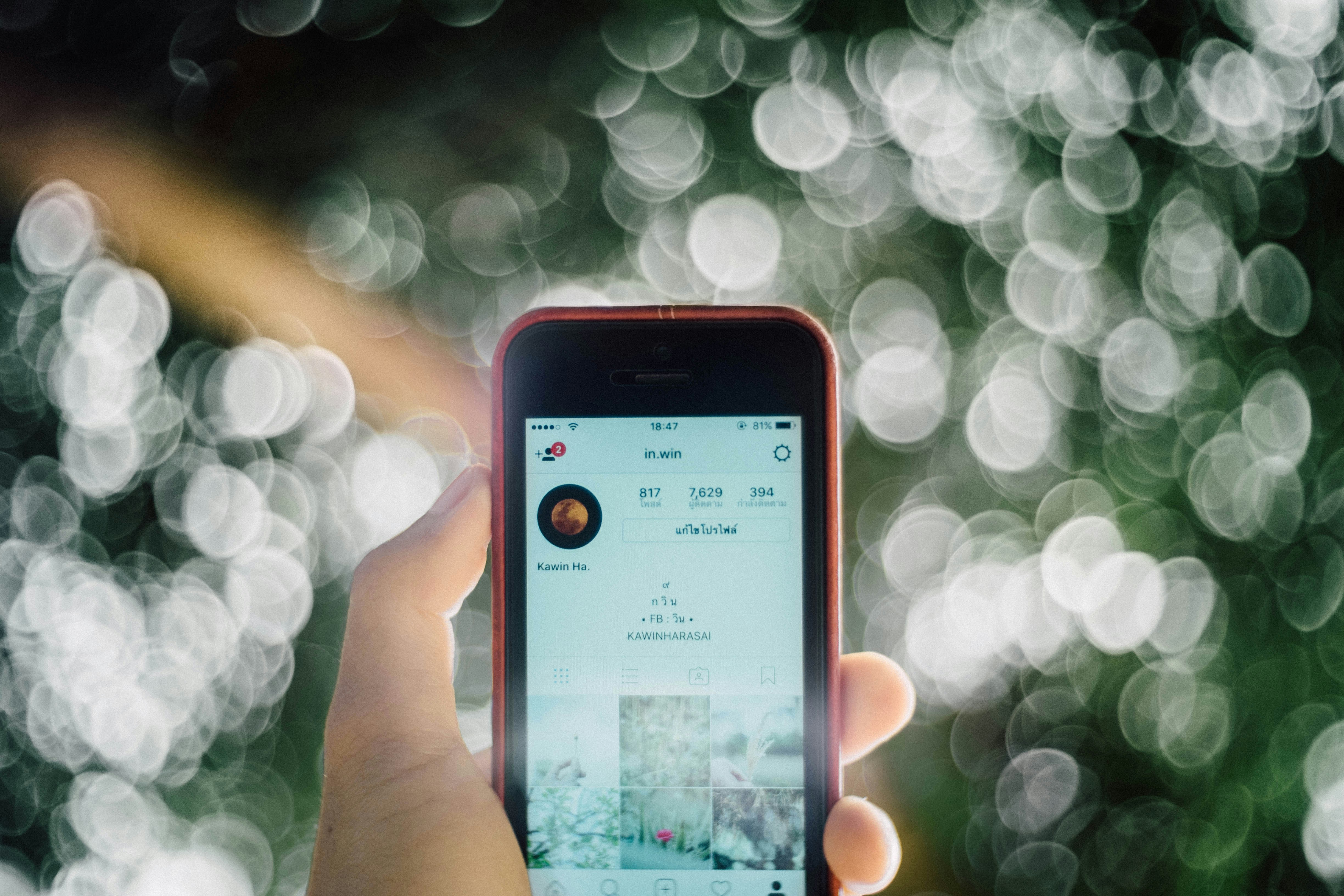 Smartphone held vertically showing social media reel, dark background, screen glow illuminating face, moody ambient lighting