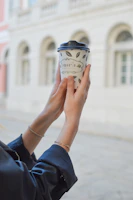 Casual street scene showing a hand adorned with yunka jewelry holding a coffee cup.